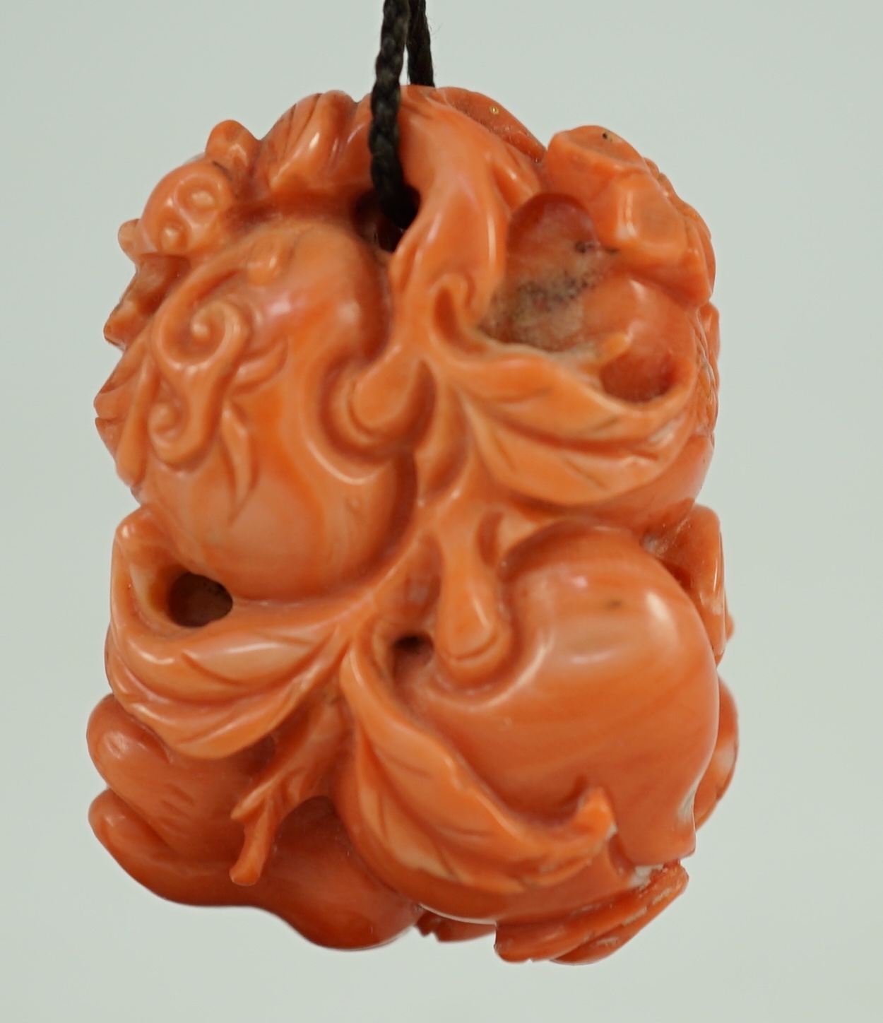 A good Chinese coral ‘fruit and bats’ pendant, 19th century, 3.7cm, later suspension stand